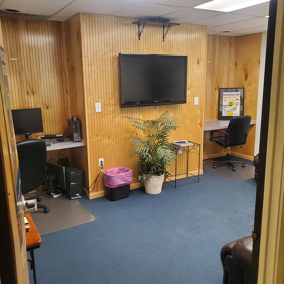 KLPR flight planning room with a desktop workstation, an open desk, and a wall-mounted TV